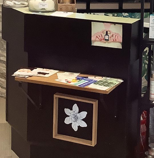 Le comptoir noir de l’accueil, avec une tablette en bois et une fleur blanche encadrée.