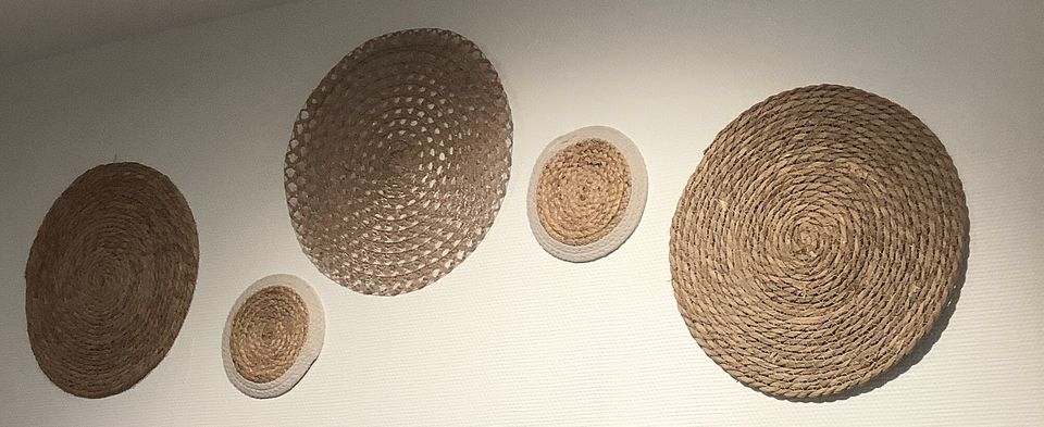 Cinq disques de rotin de tailles différentes accrochés sur un mur blanc.